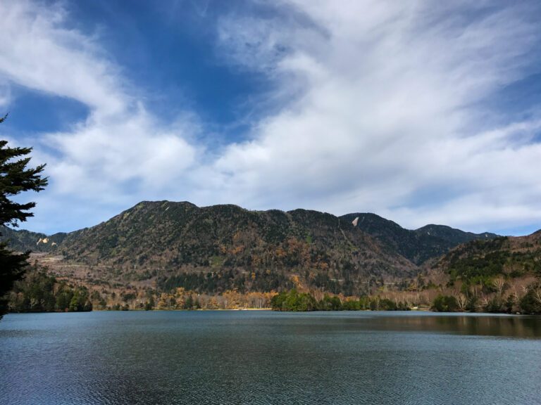 View at lake chuzenji. The mountain overlooks the body of water beneath a bright blue sky. 5 things to do in Nikko.